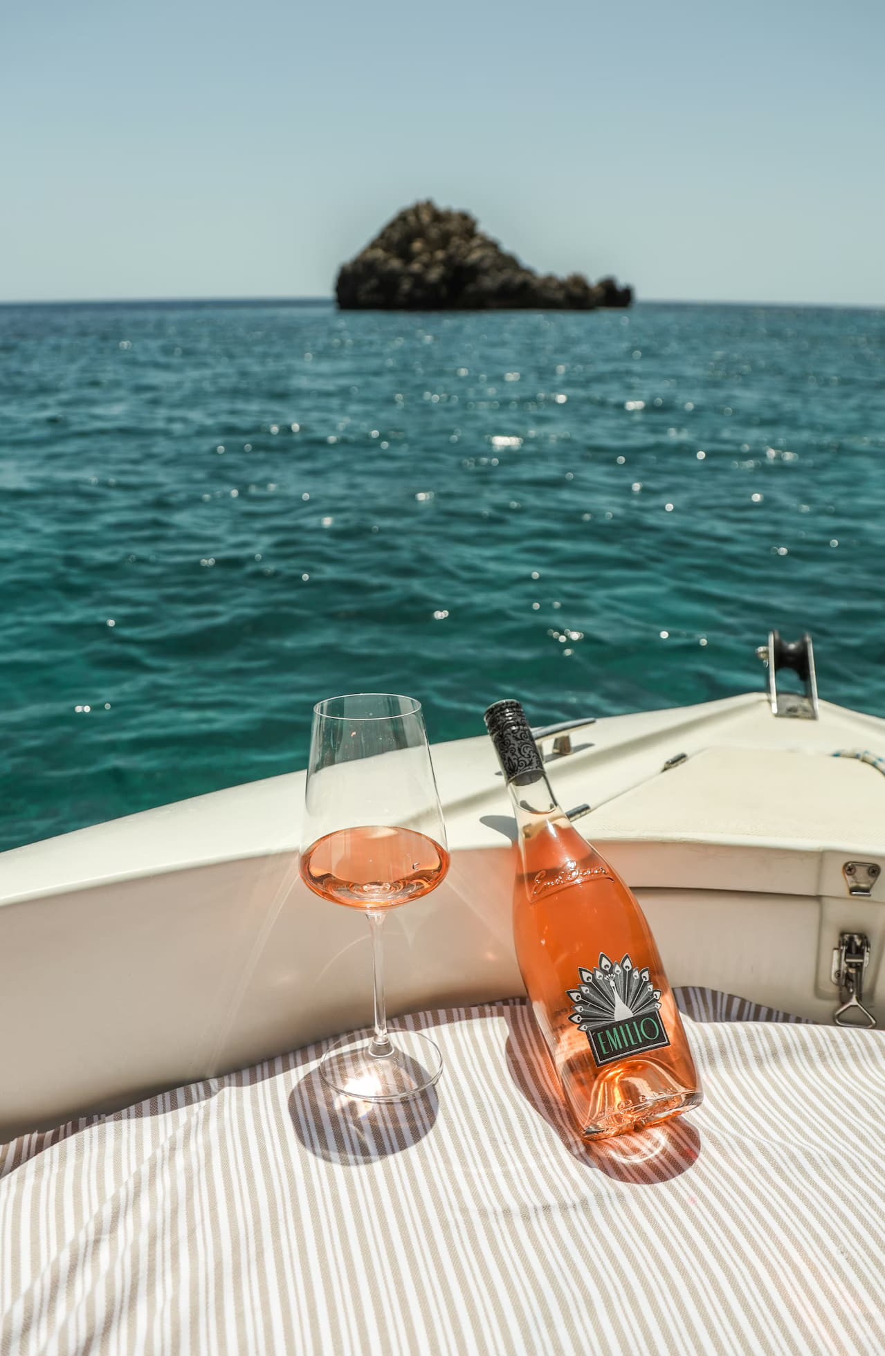 Aperitivo a bordo del gozzo davanti all'Isola di Bergeggi: rosé in calice, mare turchese, sole alto
